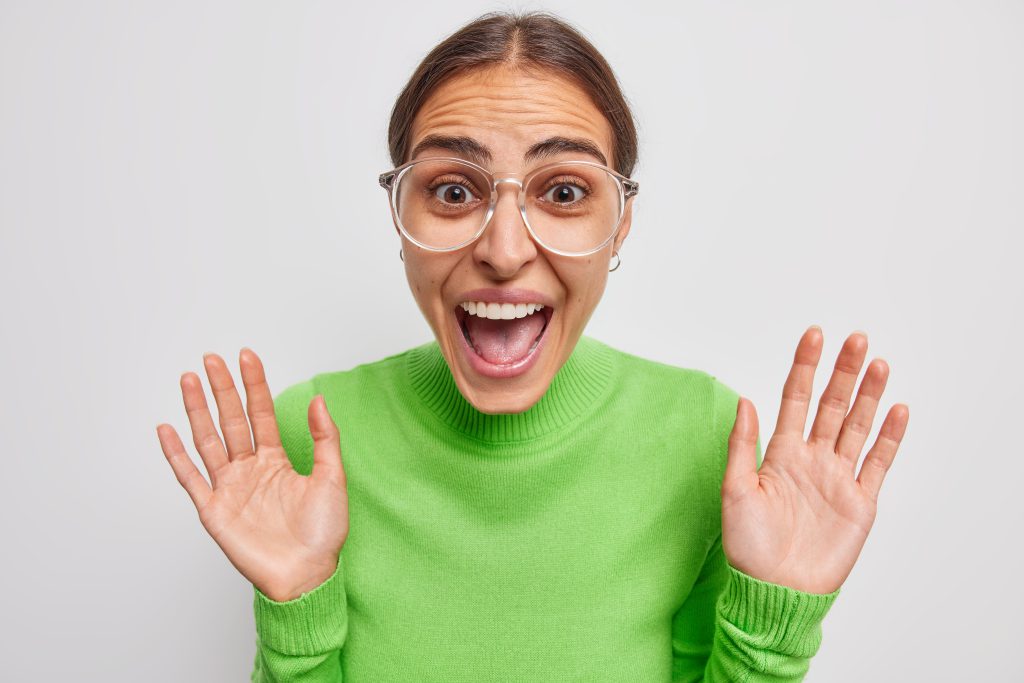 Woman wearing glasses in a green jumper looking surprised
